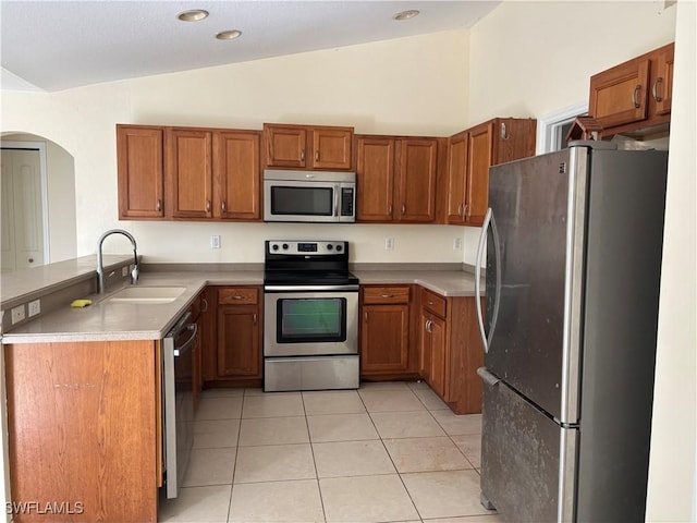 kitchen featuring brown cabinets, light tile patterned floors, appliances with stainless steel finishes, vaulted ceiling, and a sink