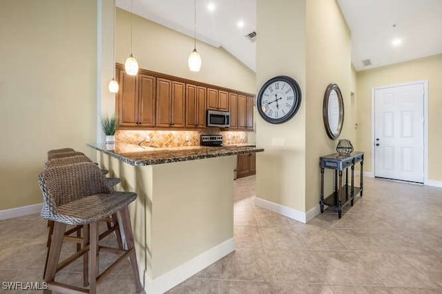 kitchen featuring brown cabinetry, a breakfast bar, dark stone countertops, stainless steel appliances, and backsplash