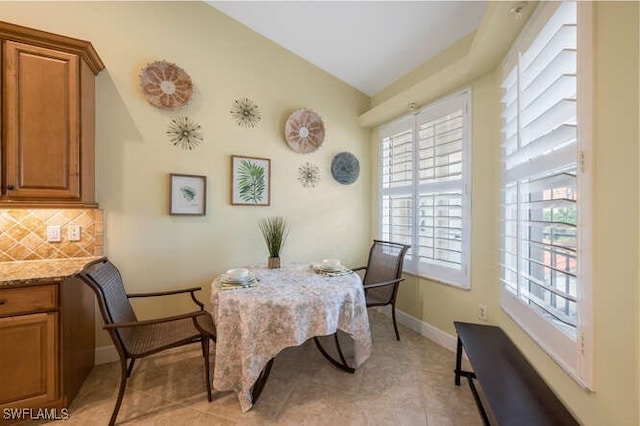 dining space featuring vaulted ceiling, light tile patterned floors, built in study area, and baseboards