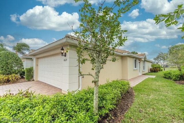 view of side of home with an attached garage, stucco siding, decorative driveway, and a yard