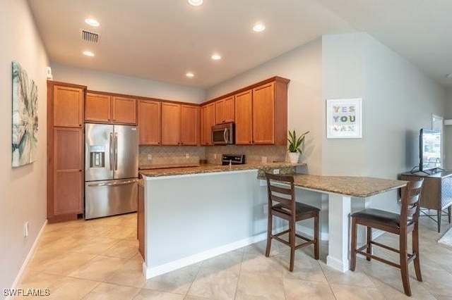 kitchen featuring visible vents, brown cabinetry, a peninsula, light stone countertops, and stainless steel appliances