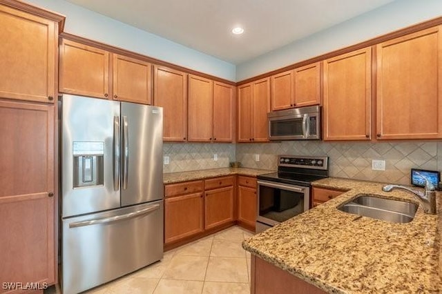 kitchen featuring appliances with stainless steel finishes, brown cabinetry, light tile patterned flooring, a sink, and light stone countertops