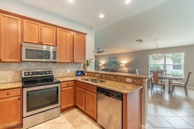 kitchen with stainless steel appliances, a peninsula, a sink, decorative backsplash, and light stone countertops