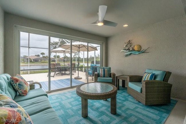 living room featuring a ceiling fan, a textured wall, a sunroom, a water view, and carpet