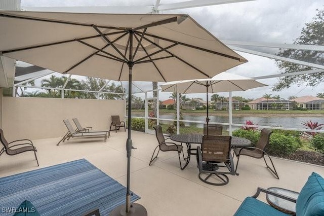 view of patio with glass enclosure, a water view, and outdoor dining area