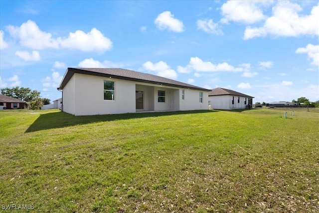 rear view of house featuring a yard and stucco siding