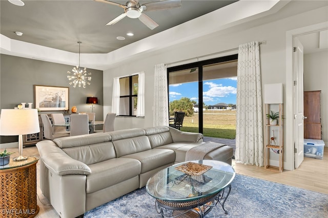 living area featuring ceiling fan with notable chandelier, a tray ceiling, wood finished floors, and recessed lighting