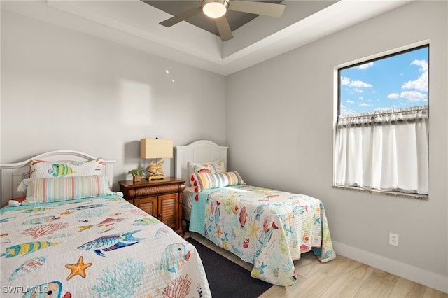 bedroom with a ceiling fan, a tray ceiling, baseboards, and wood finished floors