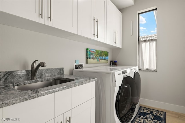 laundry area with cabinet space, baseboards, washer and dryer, light wood-style floors, and a sink