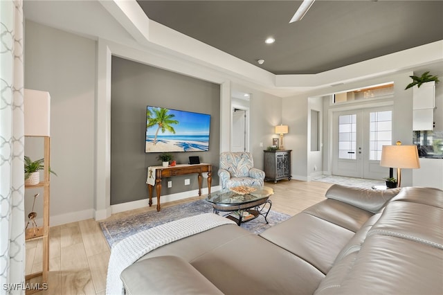 living area with a tray ceiling, french doors, light wood-type flooring, and baseboards