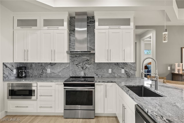 kitchen featuring wall chimney exhaust hood, appliances with stainless steel finishes, a sink, white cabinetry, and backsplash