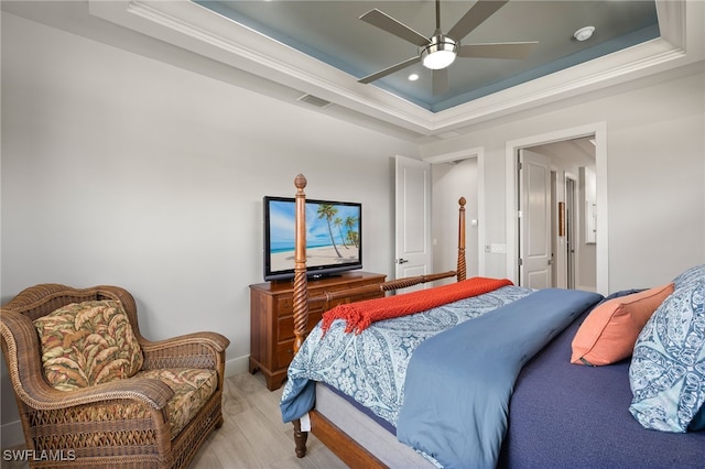 bedroom with light wood finished floors, visible vents, baseboards, ceiling fan, and a tray ceiling