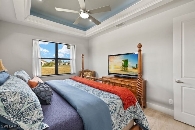 bedroom with a tray ceiling, visible vents, light wood-style floors, ceiling fan, and baseboards