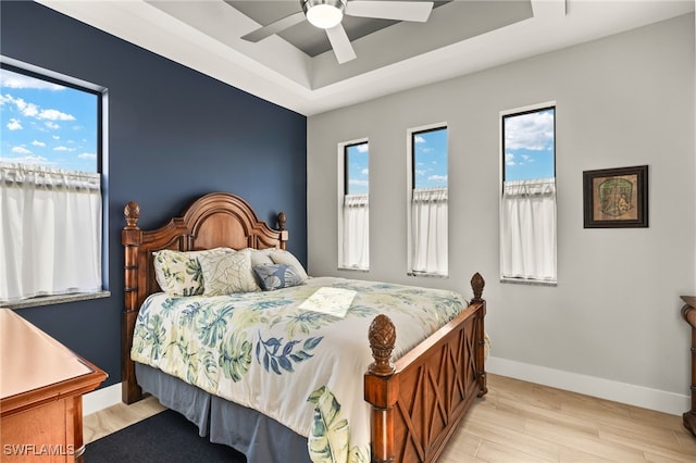 bedroom featuring a tray ceiling, ceiling fan, light wood-style flooring, and baseboards