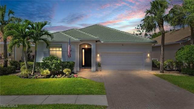 ranch-style home featuring a front yard, an attached garage, stucco siding, a tiled roof, and decorative driveway