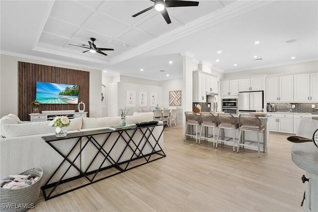 living area with ceiling fan, light wood finished floors, coffered ceiling, and ornamental molding