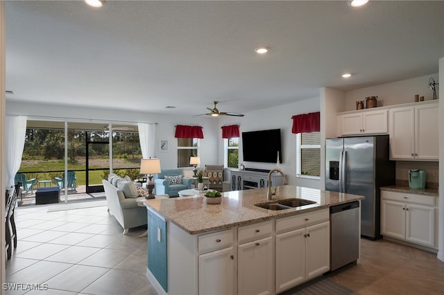 kitchen with a kitchen island with sink, a sink, white cabinetry, open floor plan, and appliances with stainless steel finishes