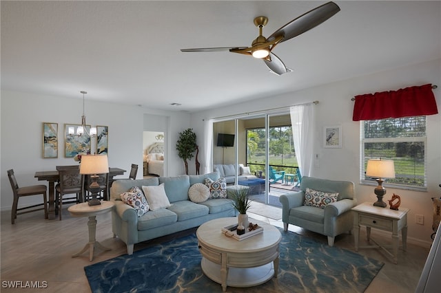 living area featuring tile patterned flooring, baseboards, and ceiling fan with notable chandelier