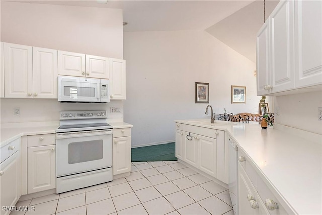 kitchen with white appliances, white cabinets, vaulted ceiling, light countertops, and a sink