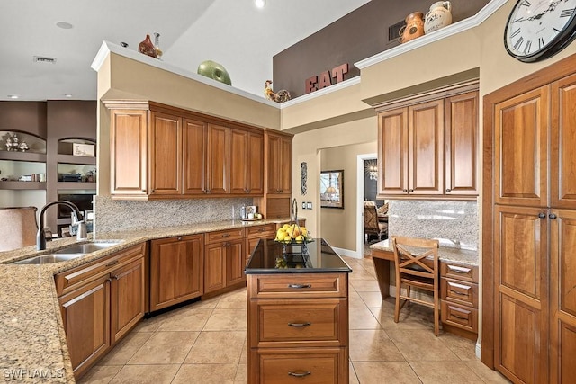 kitchen featuring light tile patterned floors, light stone countertops, a sink, backsplash, and brown cabinets