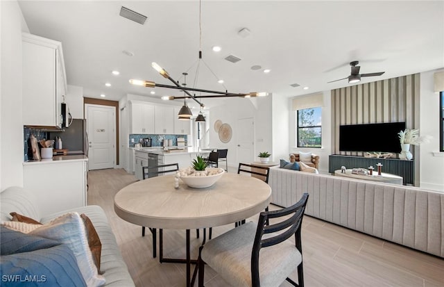 dining area with light wood-type flooring, recessed lighting, visible vents, and ceiling fan with notable chandelier