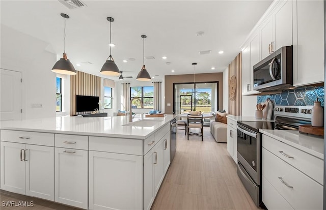 kitchen featuring stainless steel appliances, open floor plan, white cabinetry, and a sink