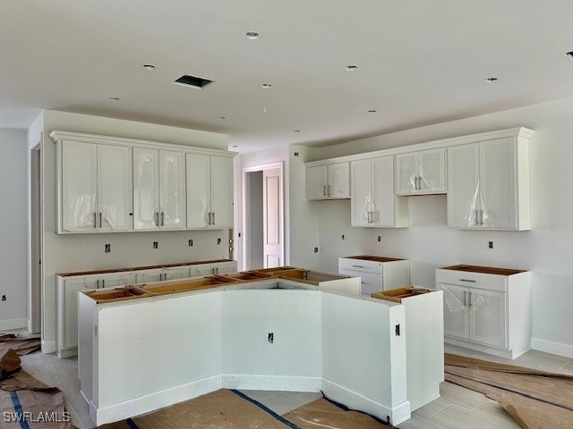 kitchen with baseboards, light wood-style floors, white cabinets, and a center island