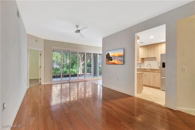 unfurnished living room with a ceiling fan, light wood-type flooring, and baseboards