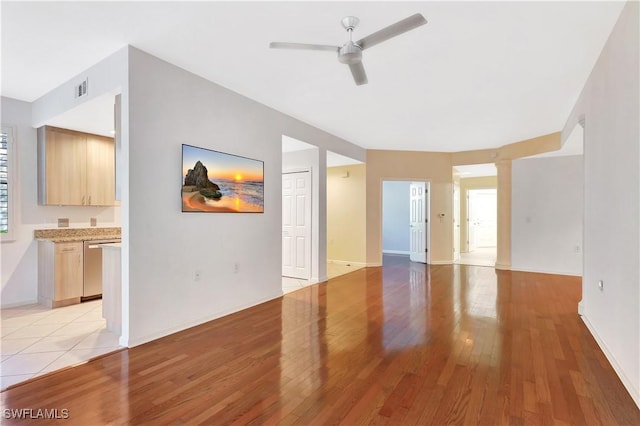 unfurnished living room featuring light wood finished floors, visible vents, baseboards, and a ceiling fan