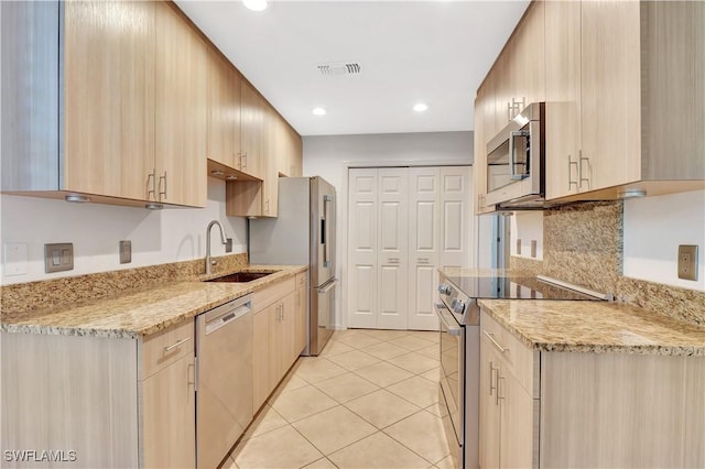 kitchen featuring visible vents, light brown cabinets, a sink, stainless steel appliances, and light stone countertops