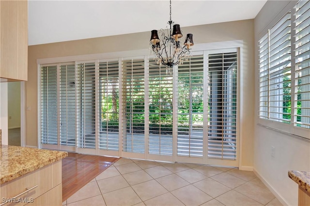 unfurnished dining area with light tile patterned floors, a notable chandelier, and baseboards