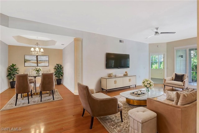 living room featuring a tray ceiling, visible vents, wood finished floors, and ceiling fan with notable chandelier