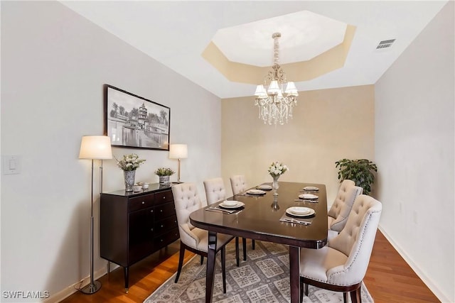 dining space featuring visible vents, a raised ceiling, baseboards, and wood finished floors