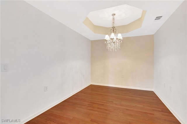 empty room with visible vents, a notable chandelier, wood finished floors, baseboards, and a raised ceiling