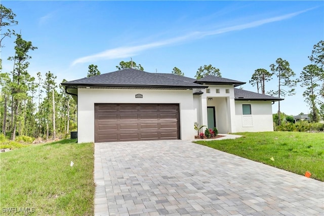 prairie-style home featuring decorative driveway, stucco siding, a shingled roof, a garage, and a front lawn