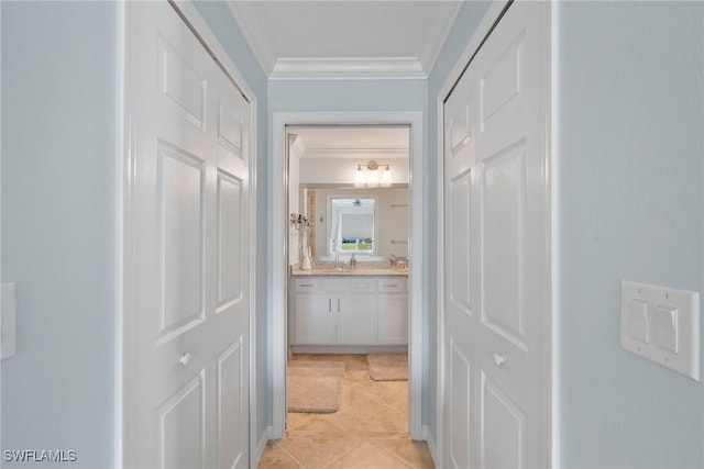 hall with light tile patterned floors, a sink, and crown molding