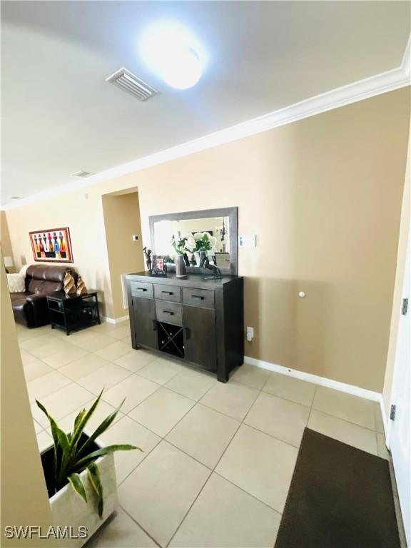 interior space with ornamental molding, light tile patterned flooring, visible vents, and baseboards