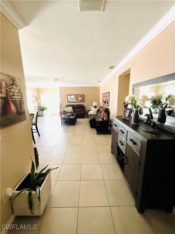 hallway with light tile patterned floors, visible vents, and crown molding