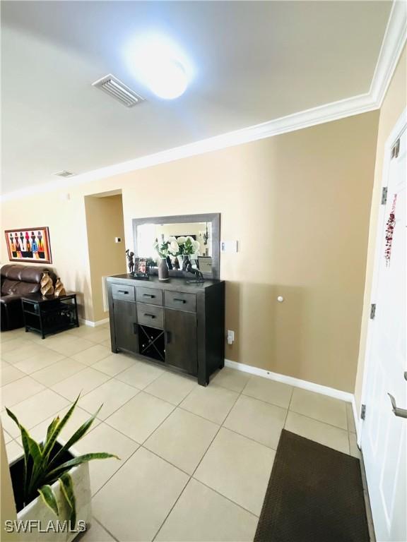 interior space featuring baseboards, light tile patterned flooring, visible vents, and crown molding