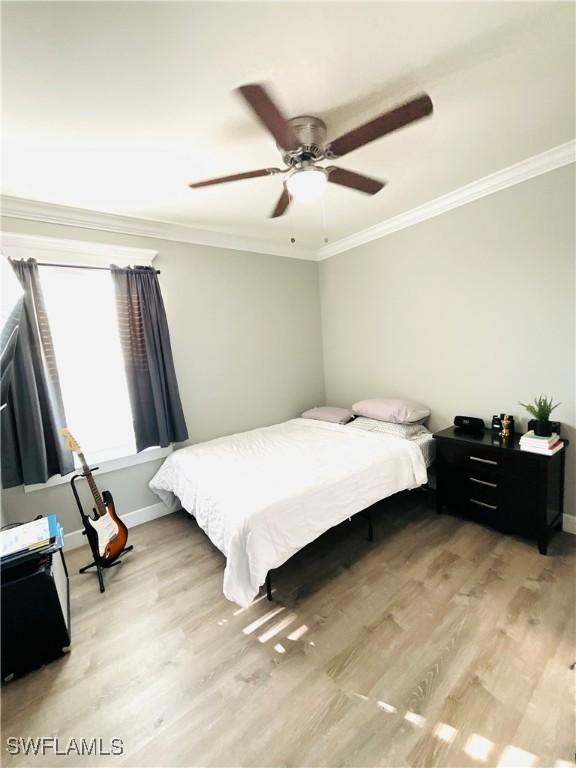 bedroom featuring ornamental molding, baseboards, light wood finished floors, and a ceiling fan