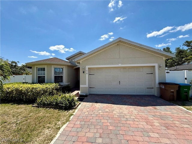 ranch-style house featuring a garage, stucco siding, fence, and decorative driveway