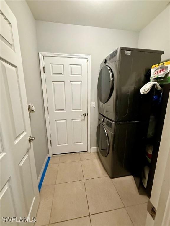washroom with light tile patterned floors, baseboards, stacked washer and clothes dryer, and laundry area