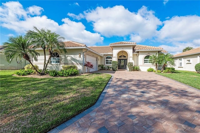 mediterranean / spanish-style home with decorative driveway, a tile roof, stucco siding, an attached garage, and a front lawn