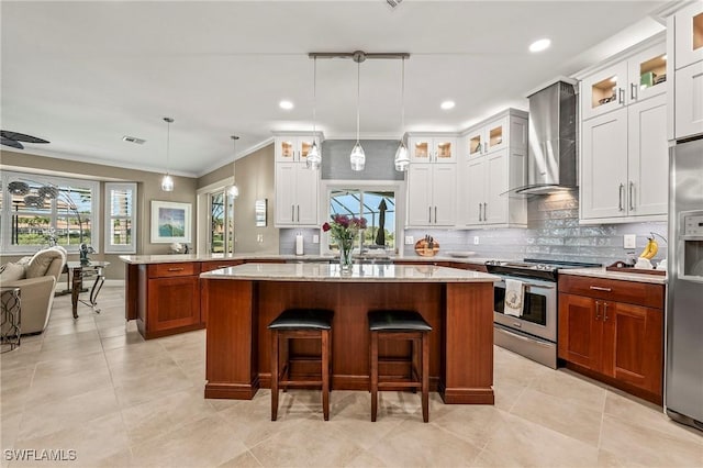 kitchen featuring wall chimney exhaust hood, a wealth of natural light, appliances with stainless steel finishes, a kitchen island, and a kitchen breakfast bar