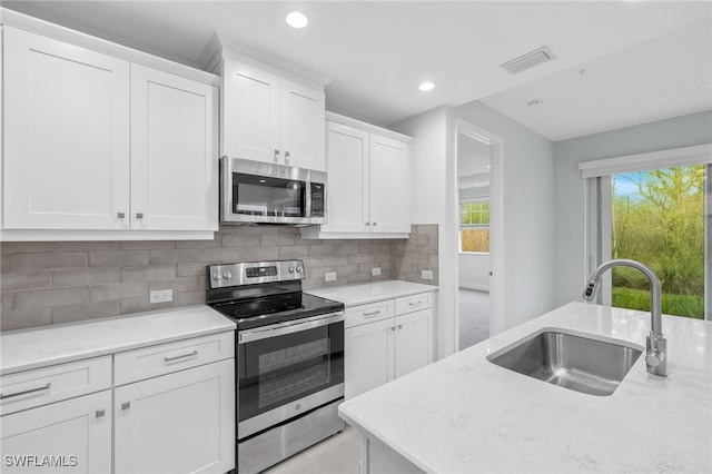 kitchen with stainless steel appliances, a sink, visible vents, white cabinetry, and tasteful backsplash