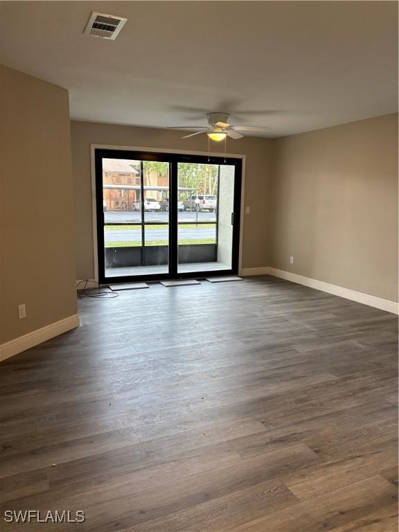 spare room with ceiling fan, visible vents, baseboards, and dark wood finished floors