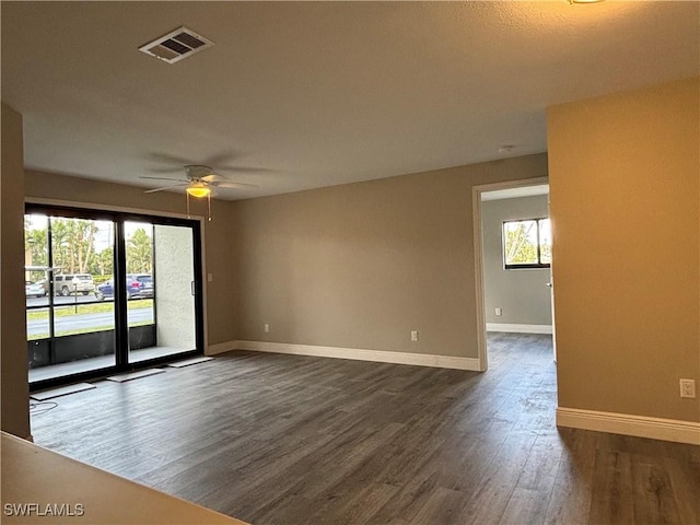 empty room featuring a wealth of natural light, visible vents, baseboards, and dark wood-style flooring