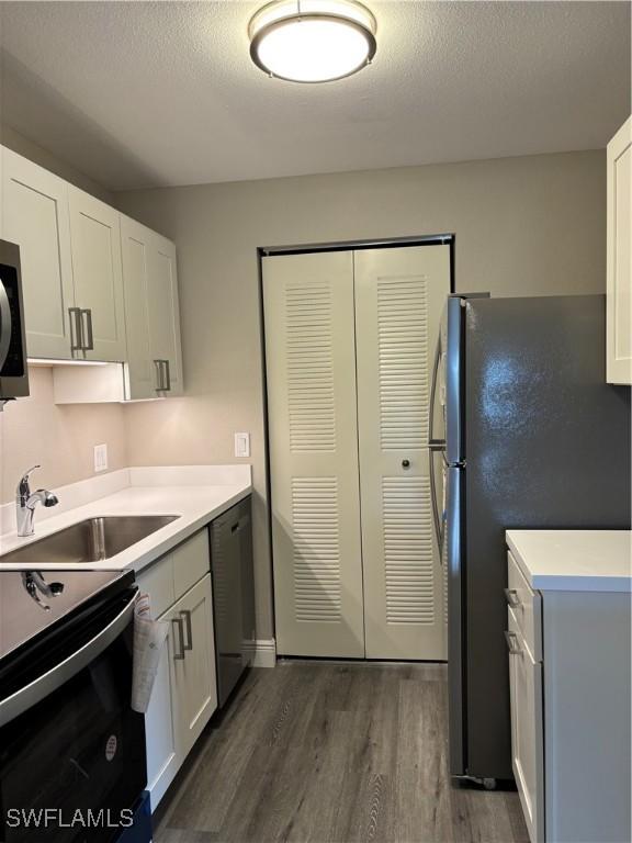 kitchen featuring light countertops, dark wood-style flooring, dishwashing machine, and a sink