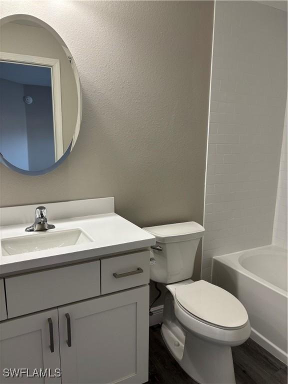 full bath with toilet, wood finished floors, vanity, and a textured wall