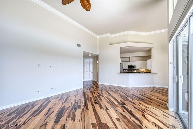 unfurnished living room with light wood-type flooring, visible vents, ornamental molding, baseboards, and a towering ceiling